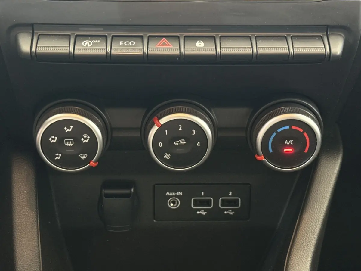 Gros plan sur les commandes de climatisation et boutons fonctionnels du tableau de bord noir de la Renault Clio blanche.
