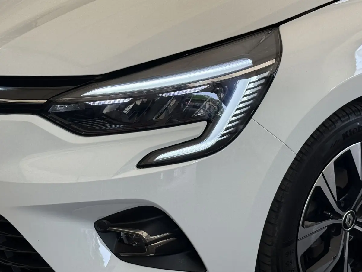 Gros plan sur le phare avant droit allumé d’une Renault Clio blanche Evolution TCe 100 GPL 2023.