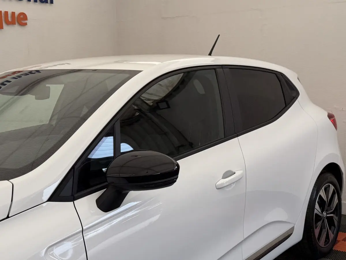 Vue latérale droite d'une Renault Clio blanche 2023 avec rétroviseur noir et vitres teintées.