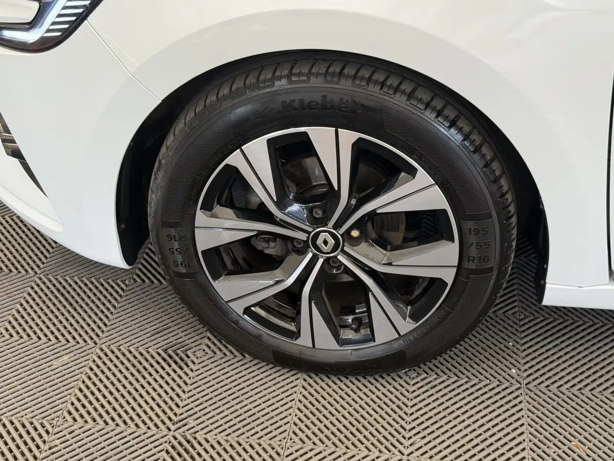 Gros plan sur la roue avant gauche d'une Renault Clio blanche avec jante alliage bicolore et logo Renault central.