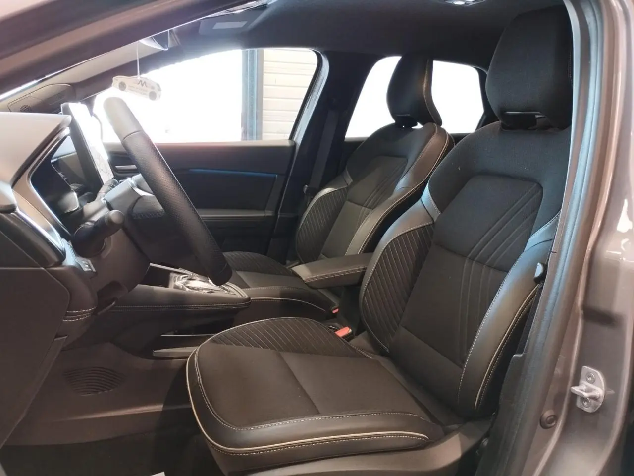 Vue intérieure côté gauche du Renault Symbioz 2025 gris Cassiope, montrant les sièges avant en tissu noir avec surpiqûres claires.