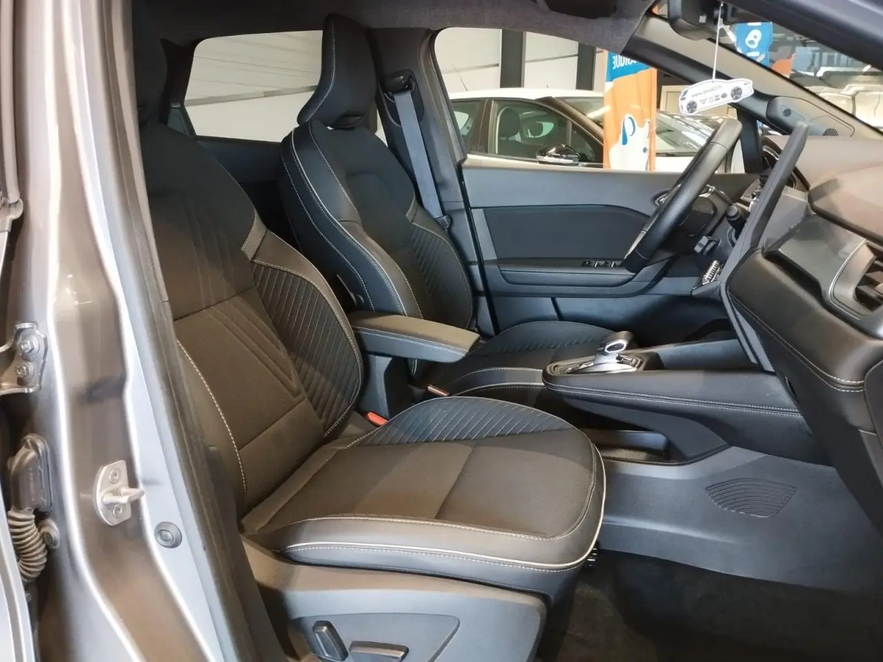 Vue intérieure côté conducteur de la Renault SYMBIOZ 1.6 E-Tech Hybride 2025 en gris Cassiopée, sièges noirs avec surpiqûres blanches.