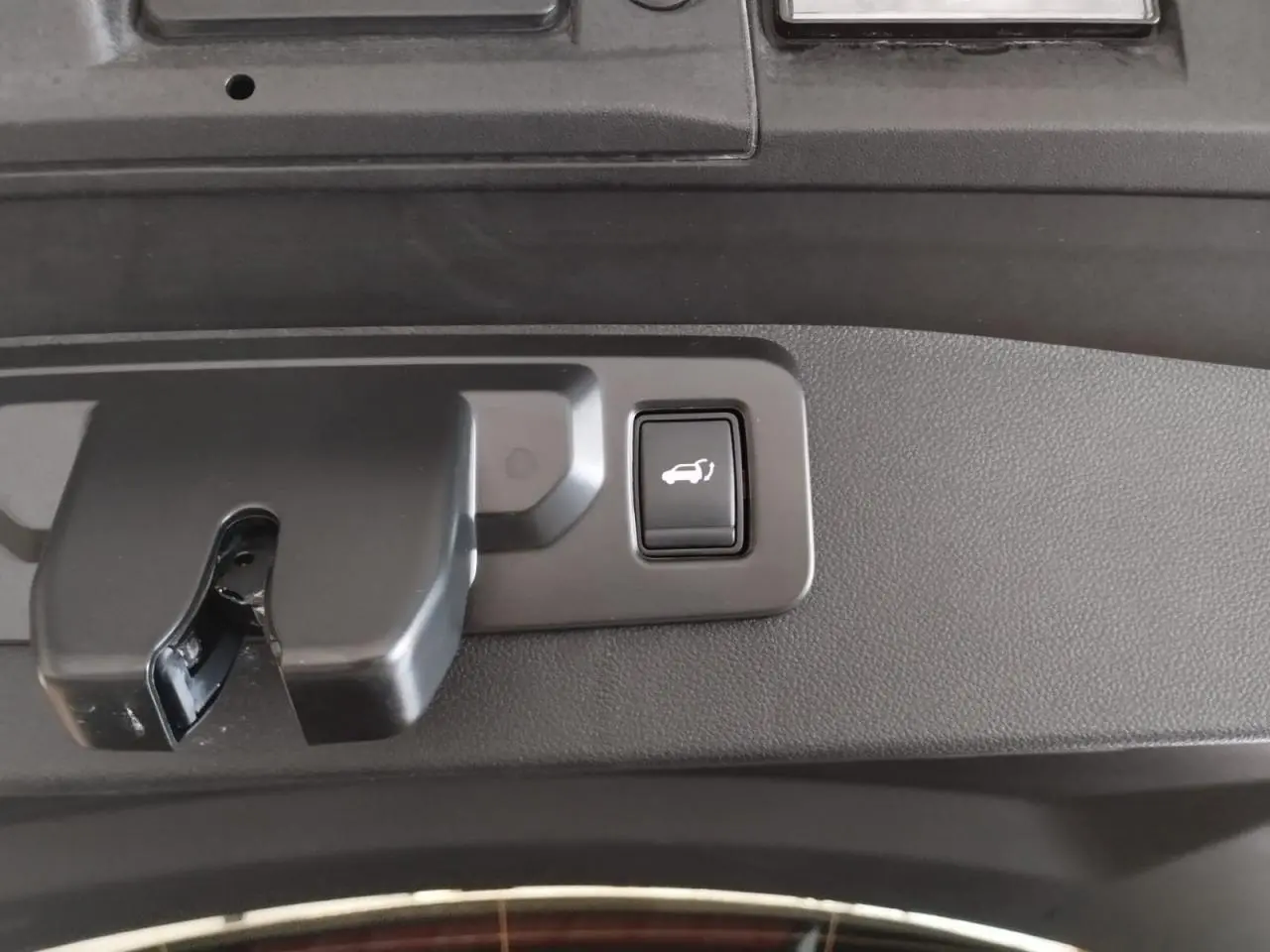 Gros plan sur le bouton d'ouverture électrique du hayon, intégré dans la garniture intérieure gris foncé du Renault Symbioz 2025.