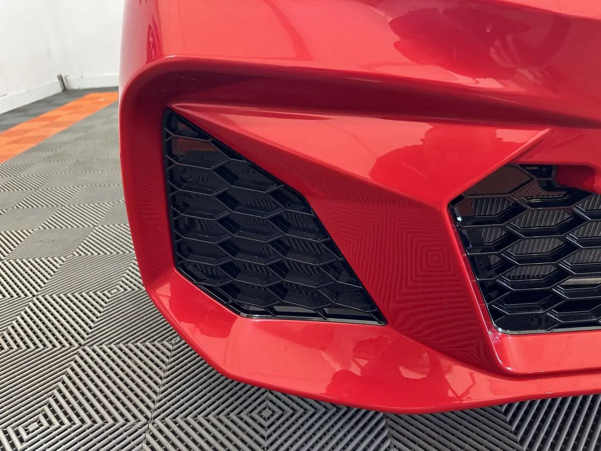 Gros plan sur la calandre avant droite rouge vif de l'AIXAM AMBITION 0.5 CITY COUPE GTI E5+ avec grille noire en nid d'abeille.