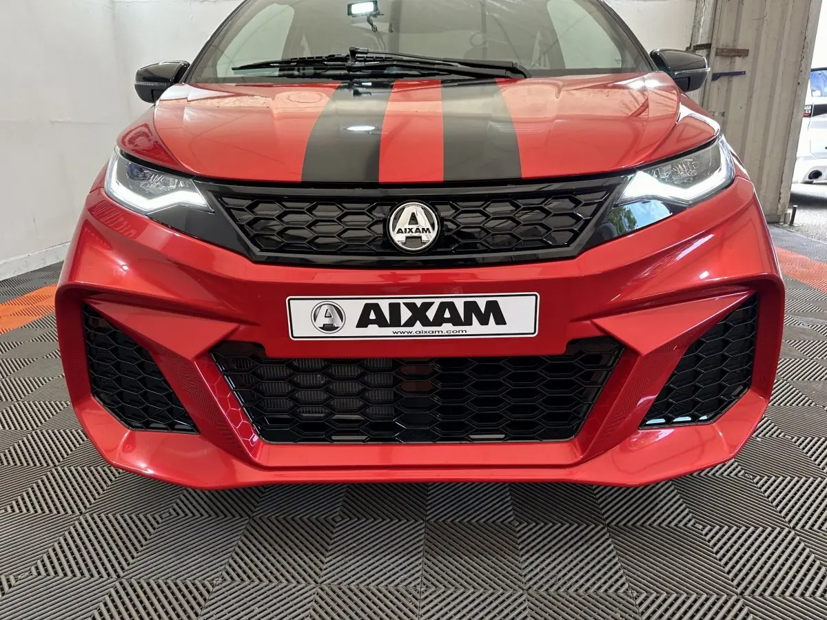 Vue avant rapprochée de l'Aixam Ambition rouge 2026 avec bandes noires et calandre hexagonale distinctive.