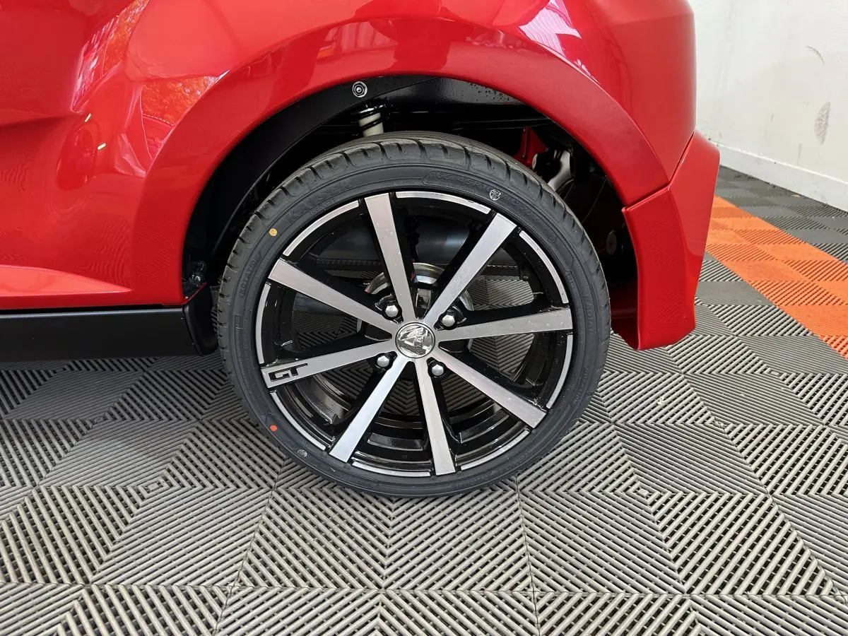 Gros plan sur la roue arrière droite rouge d'une Aixam Ambition 0.5 City Coupe GTI avec jante noire et argentée GT.