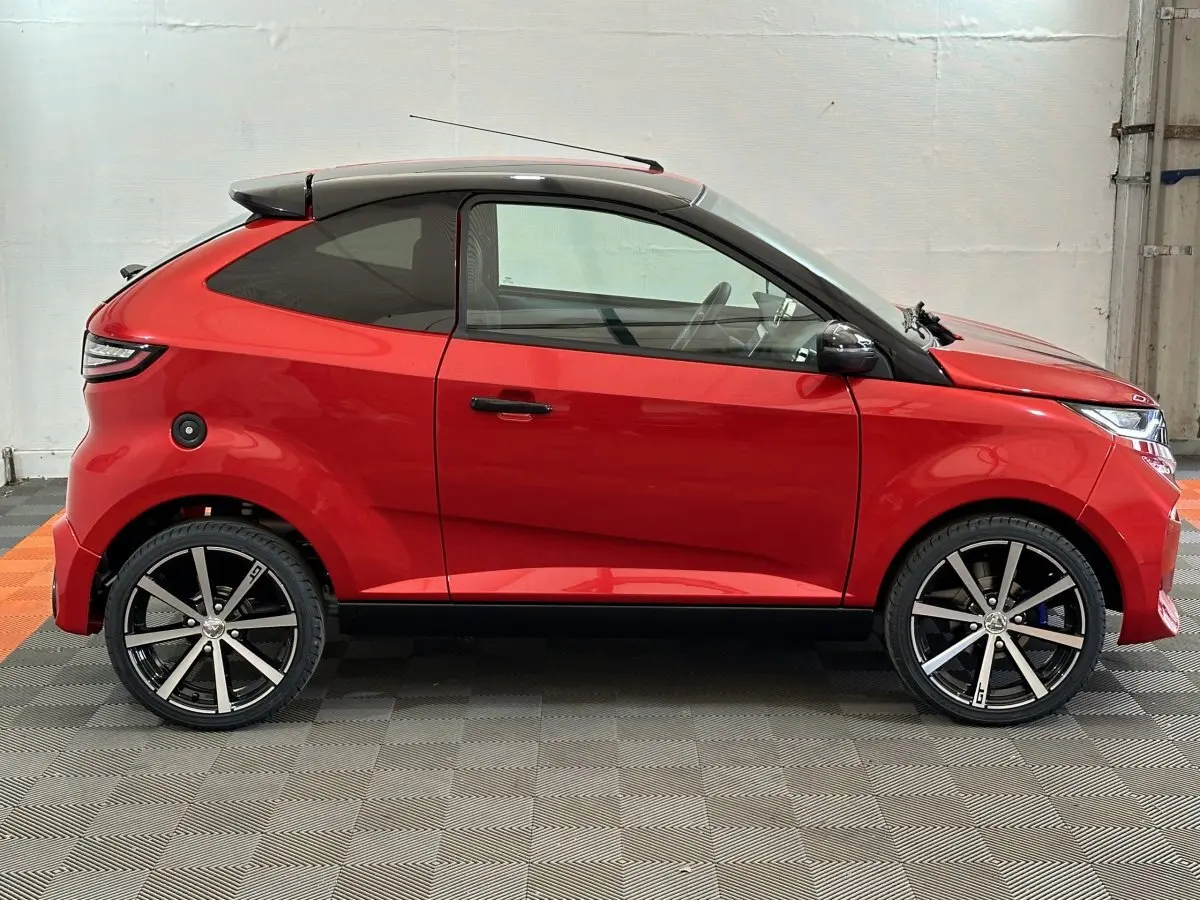 Vue de profil droit de l'AIXAM AMBITION 0.5 CITY COUPE GTI E5+ rouge avec toit noir et jantes alliage distinctives.