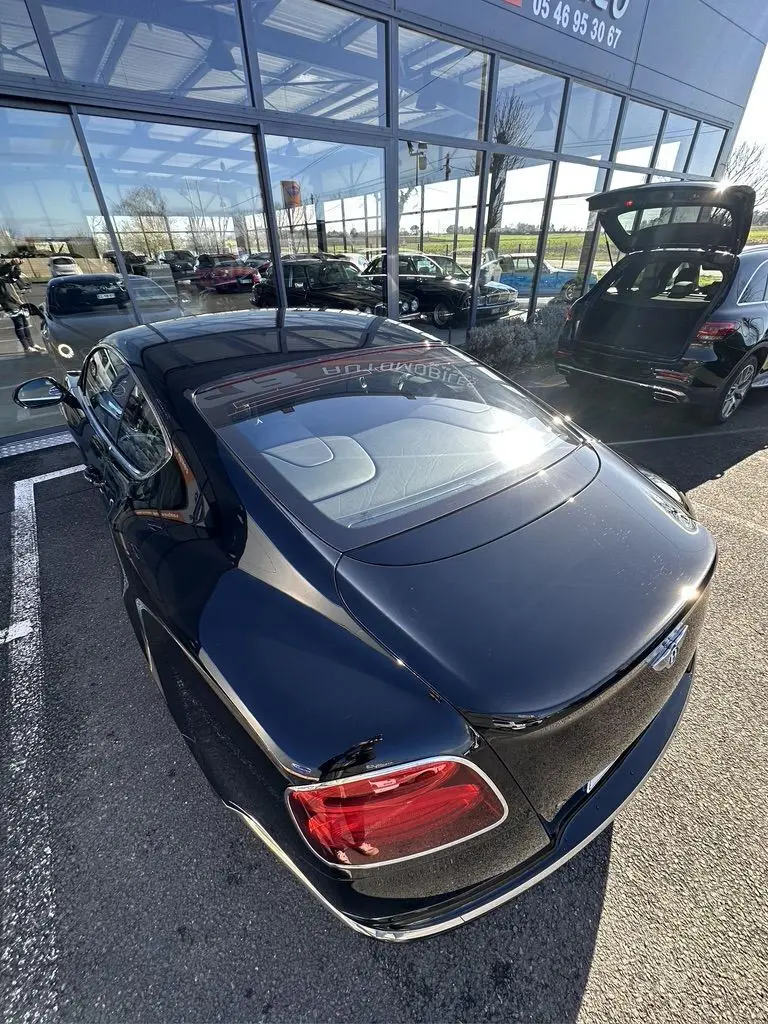 Vue 3/4 arrière haute d'une Bentley Continental GT Speed noire brillante avec feux arrière rouges et toit vitré.