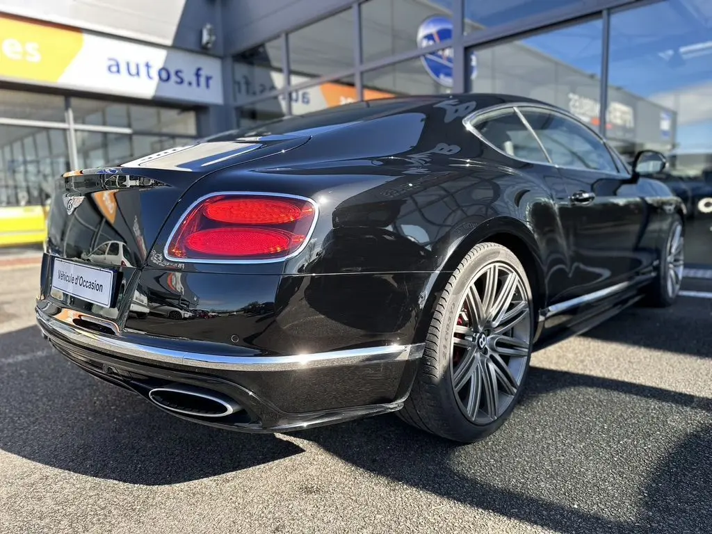Vue 3/4 arrière droite d'une Bentley Continental GT Speed noire de 2015 avec jantes alliage et feux arrière rouges.