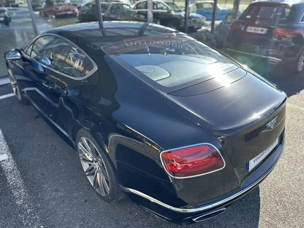 Vue 3/4 arrière droite d'une Bentley Continental GT Speed noire de 2015 avec feux arrière rouges et jantes alliage.