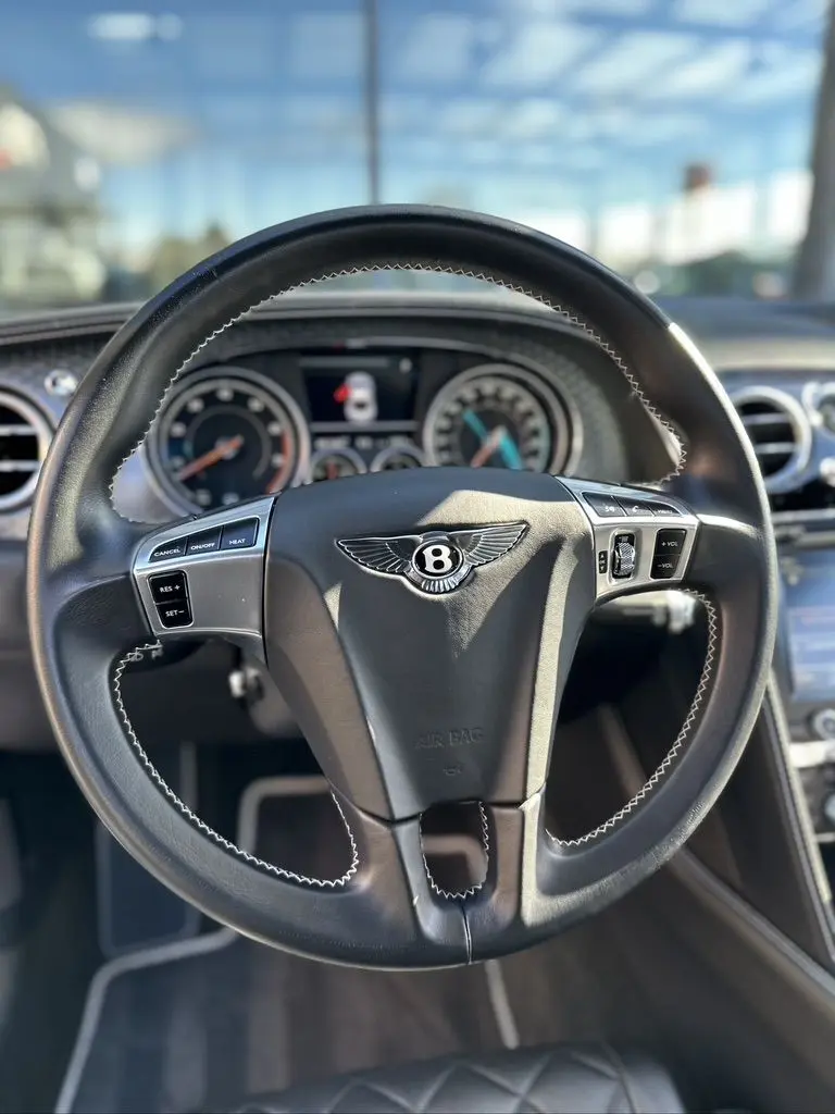 Vue rapprochée du volant noir en cuir avec logo Bentley, tableau de bord et commandes intégrées visibles à l'intérieur d'une Continental GT 2015.
