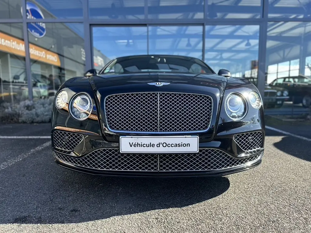 Vue frontale d'une Bentley Continental GT Speed noire 2015 avec calandre en maille chromée et phares ronds allumés.
