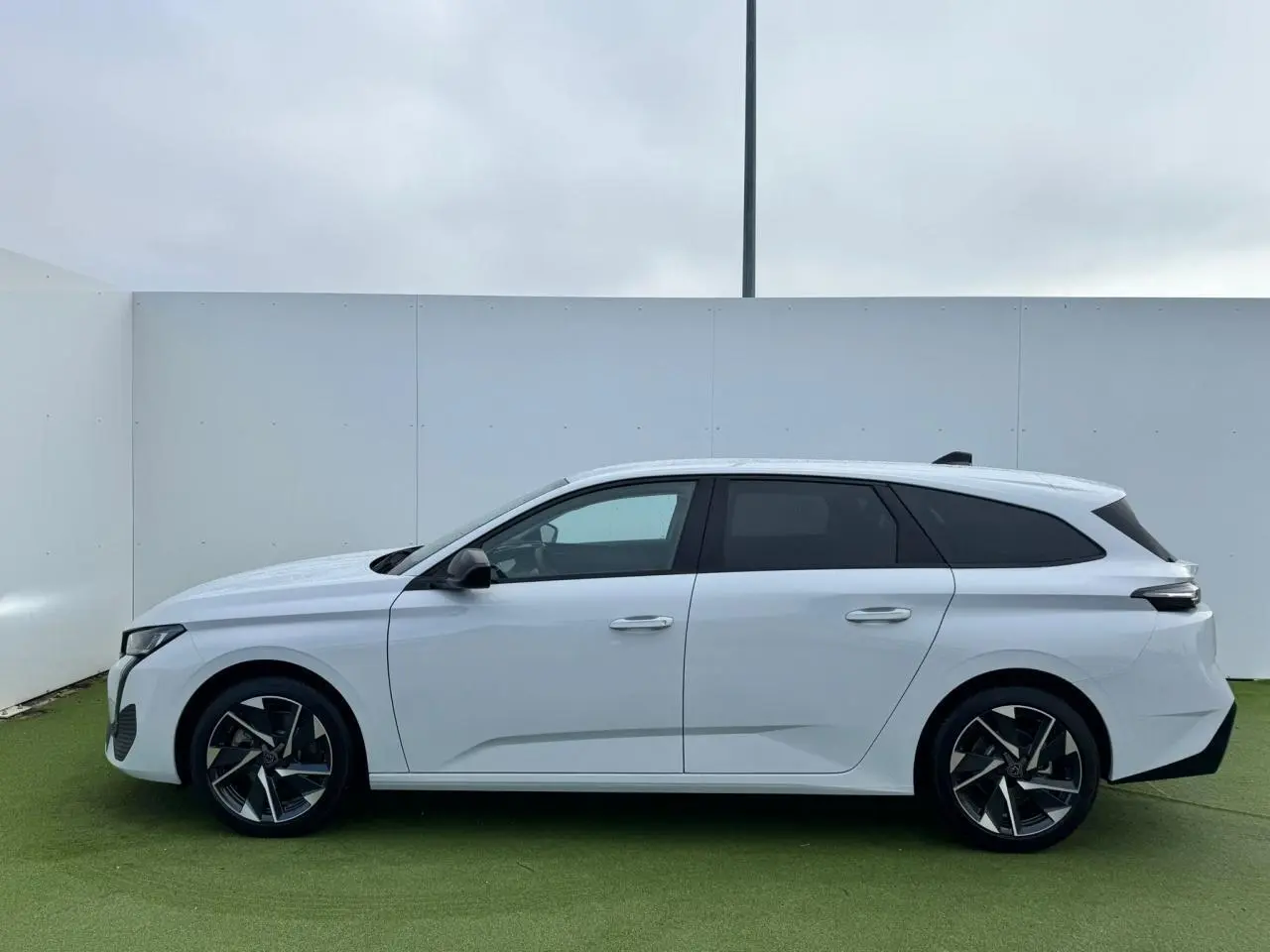 Profil latéral droit d'une Peugeot 308 SW 2024 blanche Okenite avec jantes alliage 17'' Halong diamantées et vitres surteintées.