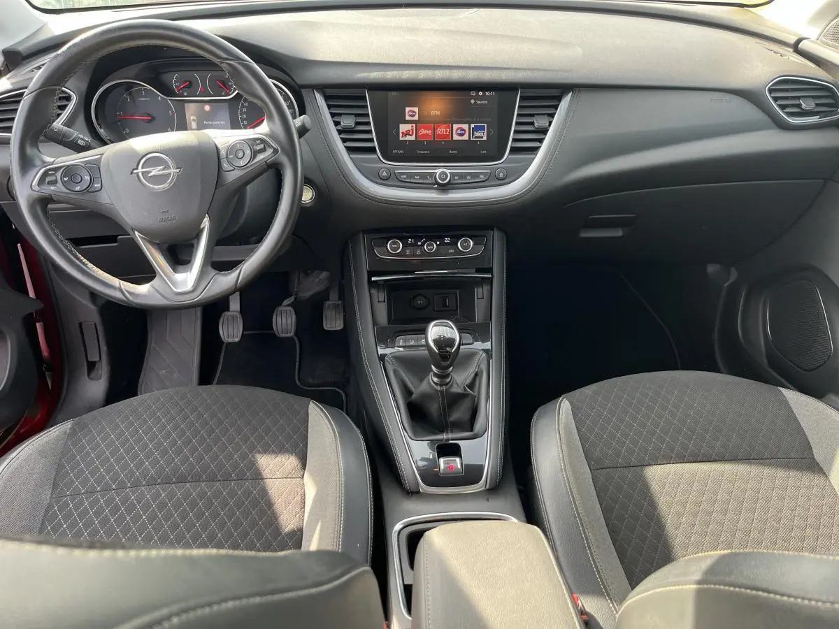 Vue intérieure avant de l'Opel Grandland rouge 2018, volant cuir, boîte manuelle, écran tactile et sièges tissu noir.