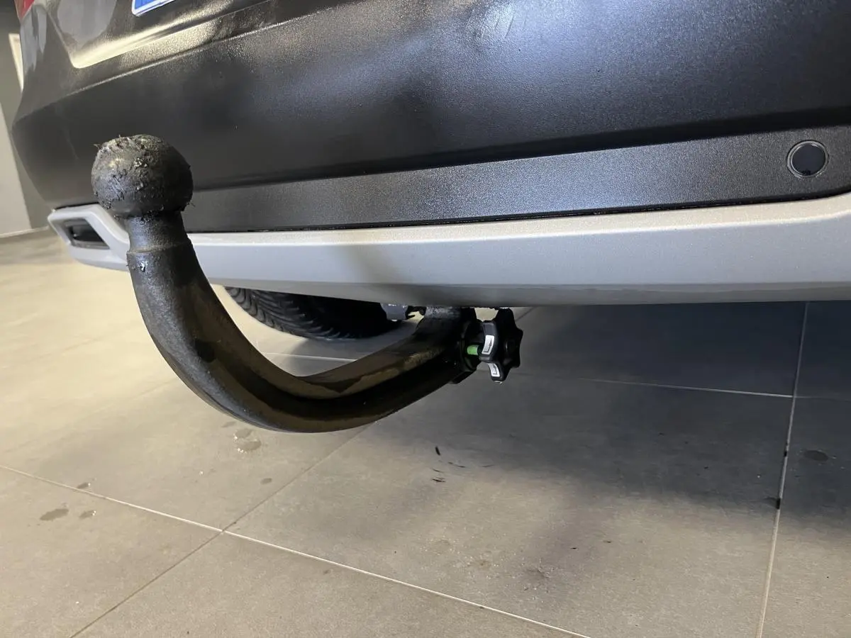 Gros plan sur le crochet d'attelage amovible noir sous le pare-chocs arrière gris d'un Opel Grandland rouge.