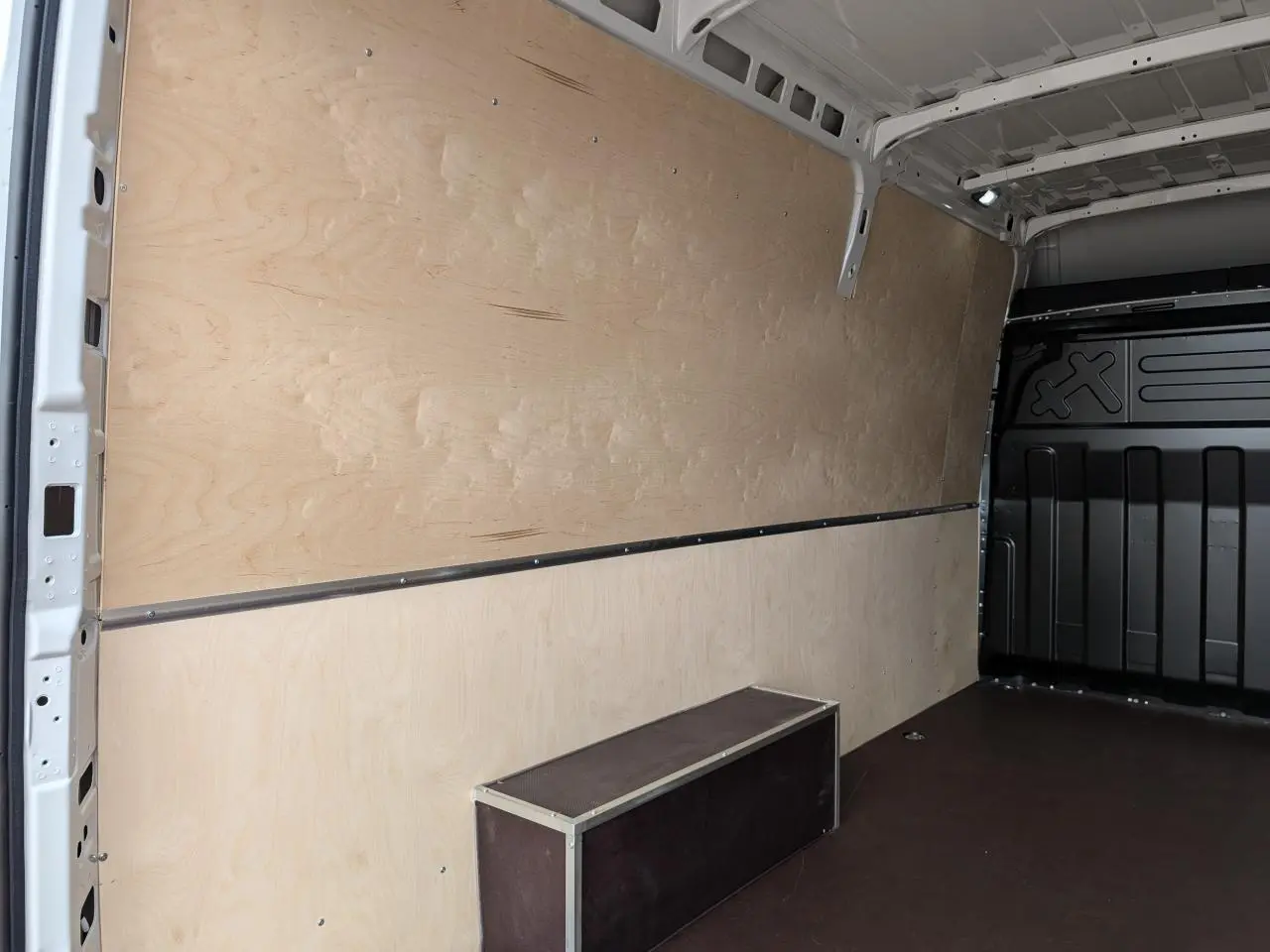 Intérieur du coffre du fourgon Iveco Daily blanc, vue latérale gauche montrant les habillages bois et plancher anti-dérapant.
