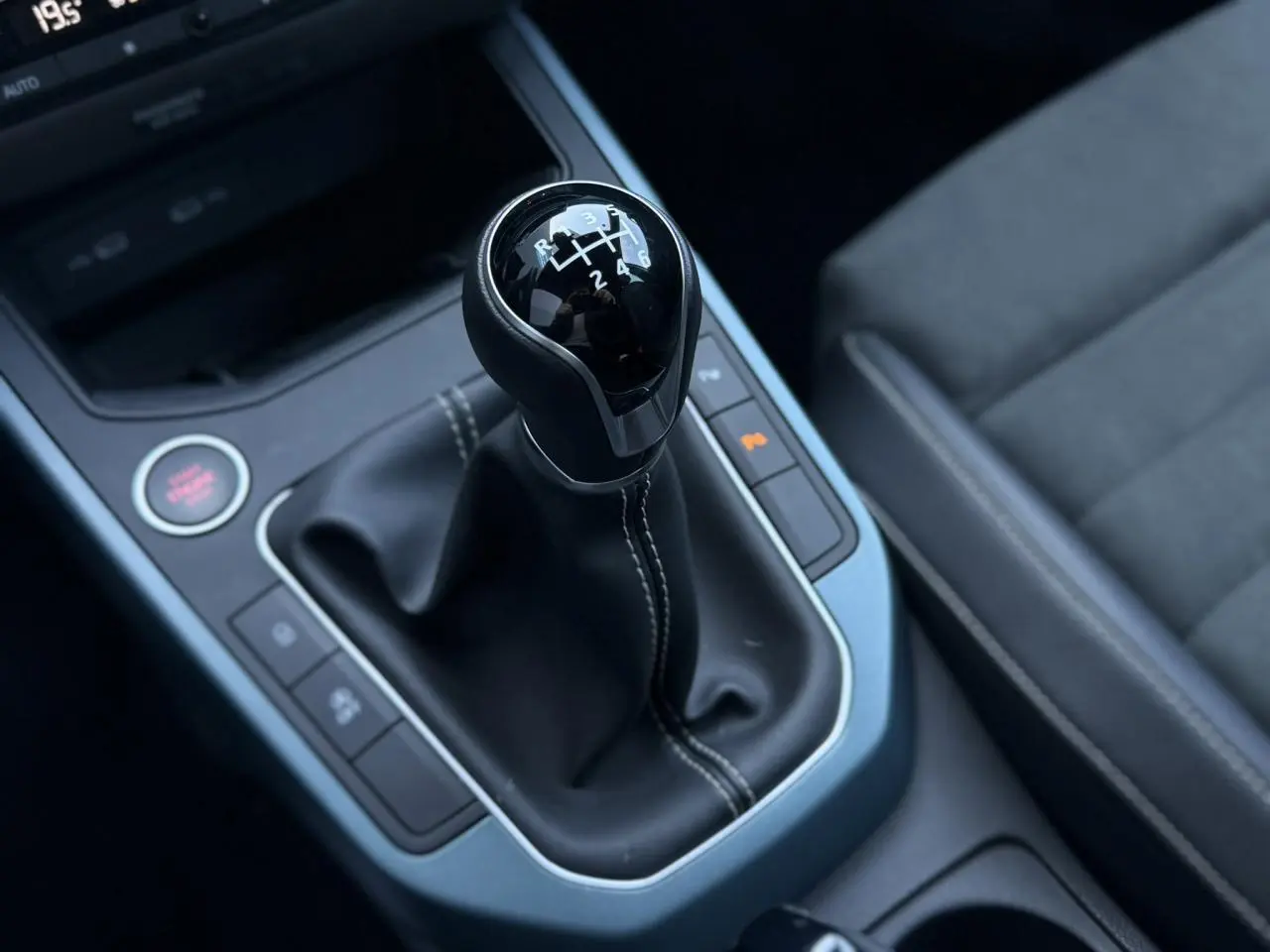 Gros plan sur le levier de vitesse manuel noir avec coutures blanches et sellerie suédine grise du SEAT Arona TSI 115 Xpérience.