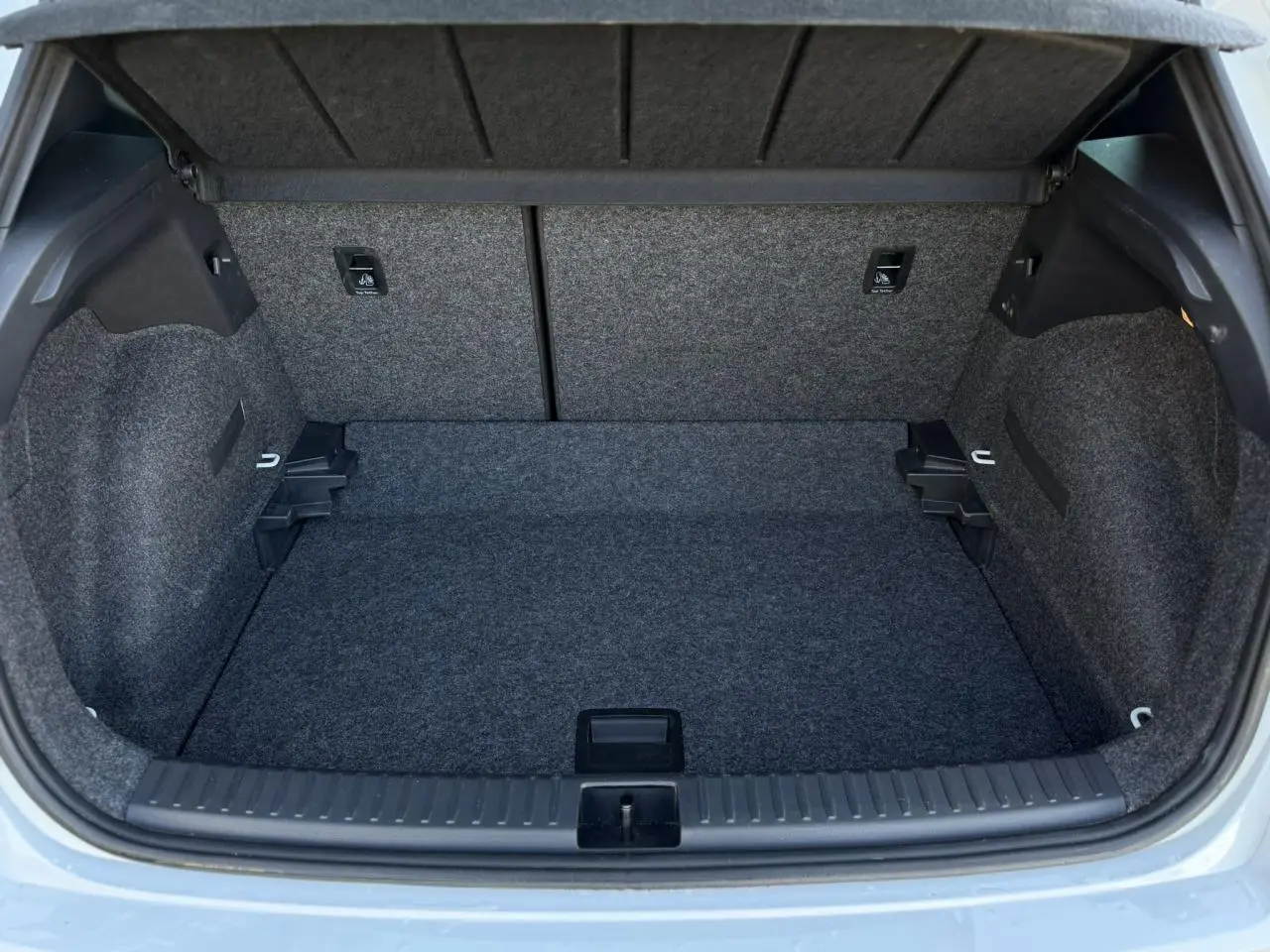 Coffre ouvert vu de l'arrière d'un SEAT Arona blanc Nevada, montrant un espace de chargement vide et doublé de moquette grise.