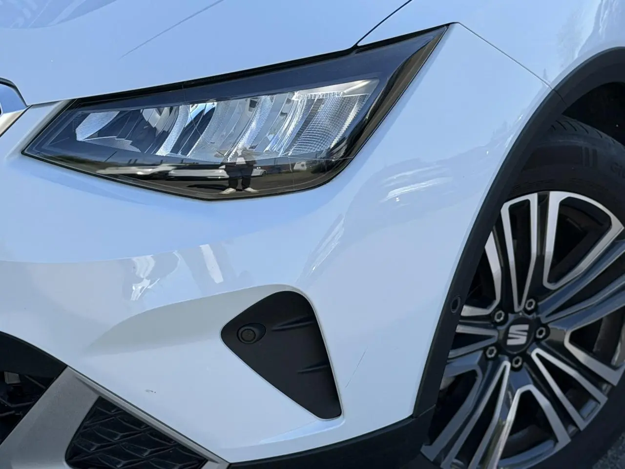 Gros plan sur l'avant droit du SEAT Arona blanc Nevada, mettant en valeur le phare LED et la jante alliage 17 pouces.