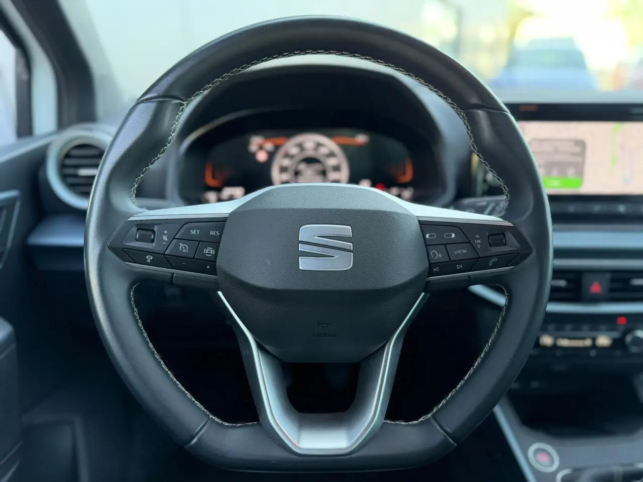 Vue rapprochée du volant cuir noir du SEAT Arona 2025 avec commandes intégrées et tableau de bord digital flou en arrière-plan.