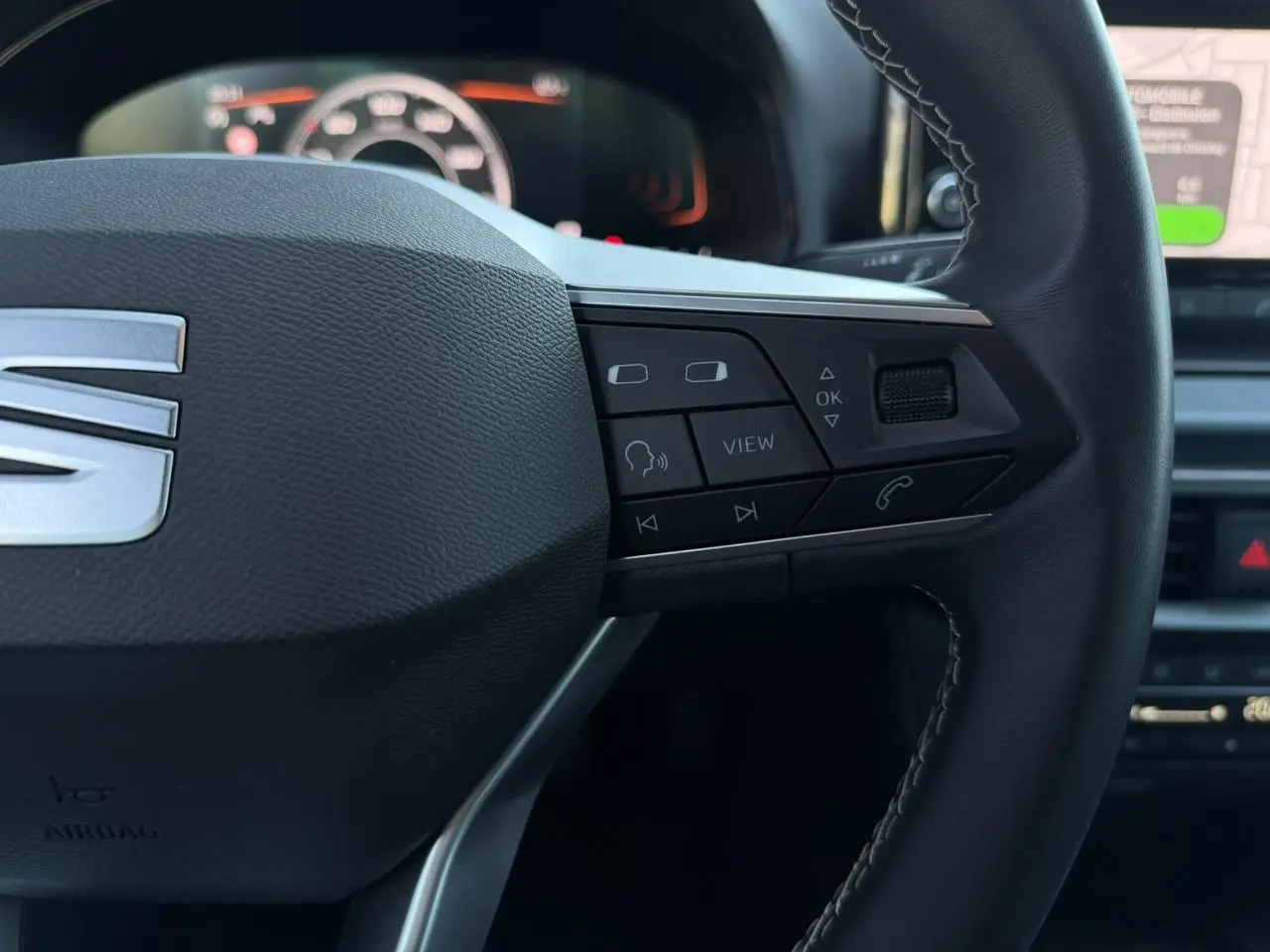 Gros plan sur le côté droit du volant noir du SEAT Arona avec commandes multifonctions et tableau de bord digital en arrière-plan.