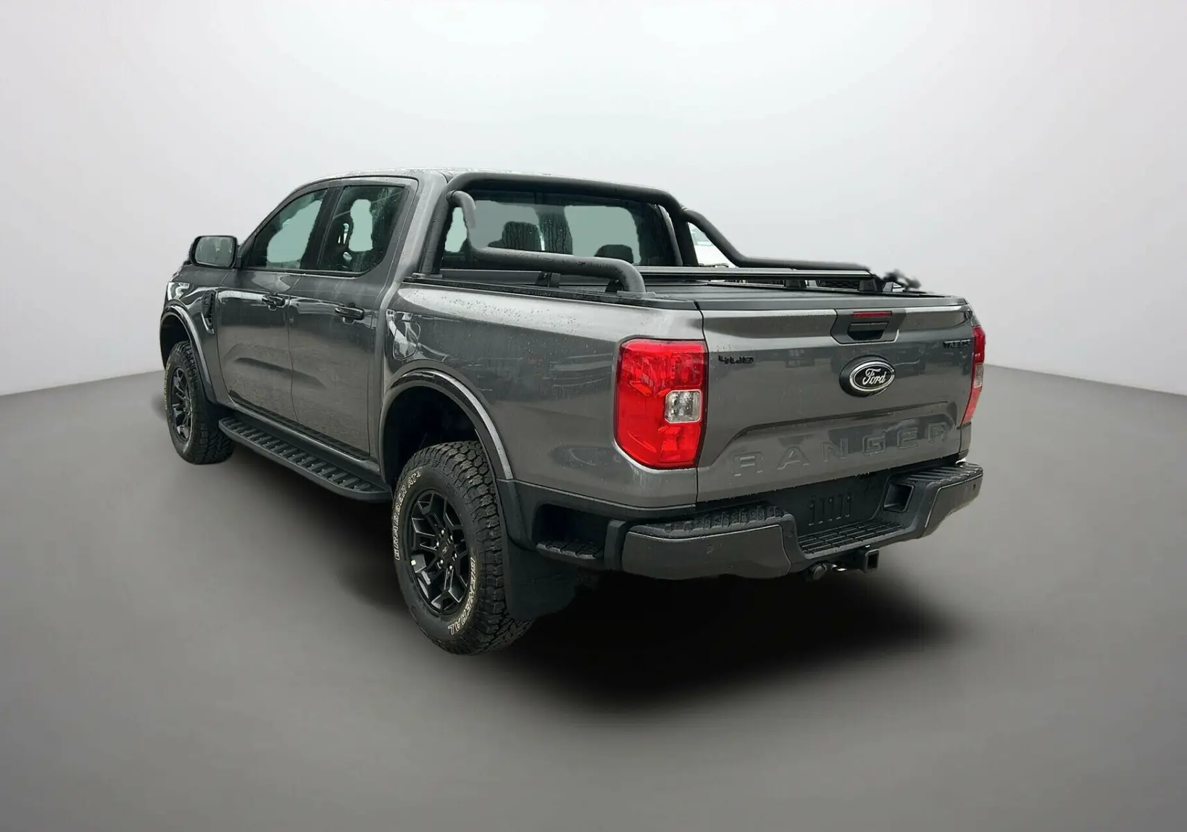 Ford Ranger gris carbone en 3/4 arrière droit, avec arceaux noirs et attelage visible sur la benne.