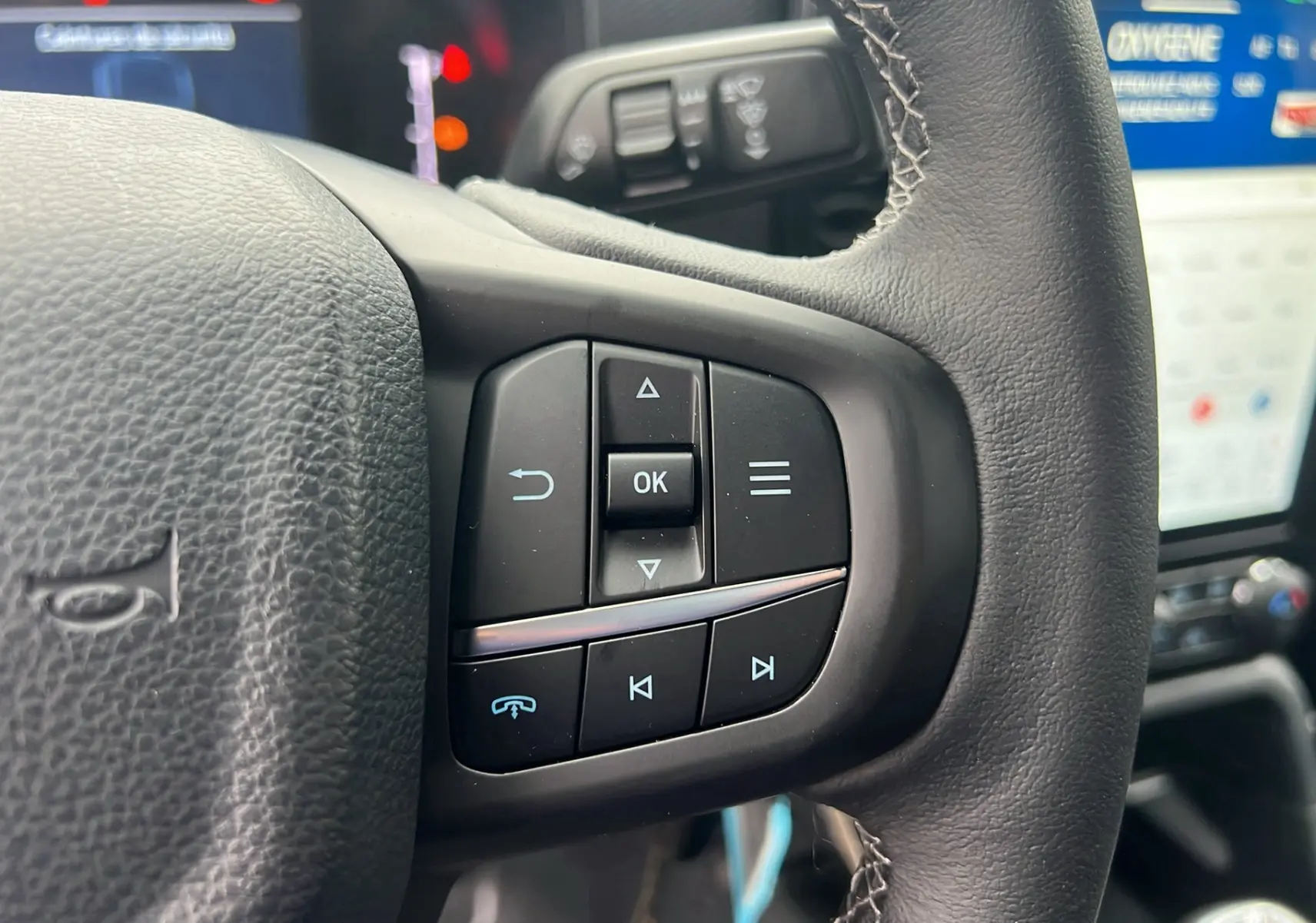 Gros plan sur le volant cuir multifonctions du Ford Ranger 2025, avec commandes audio et écran tactile en arrière-plan.
