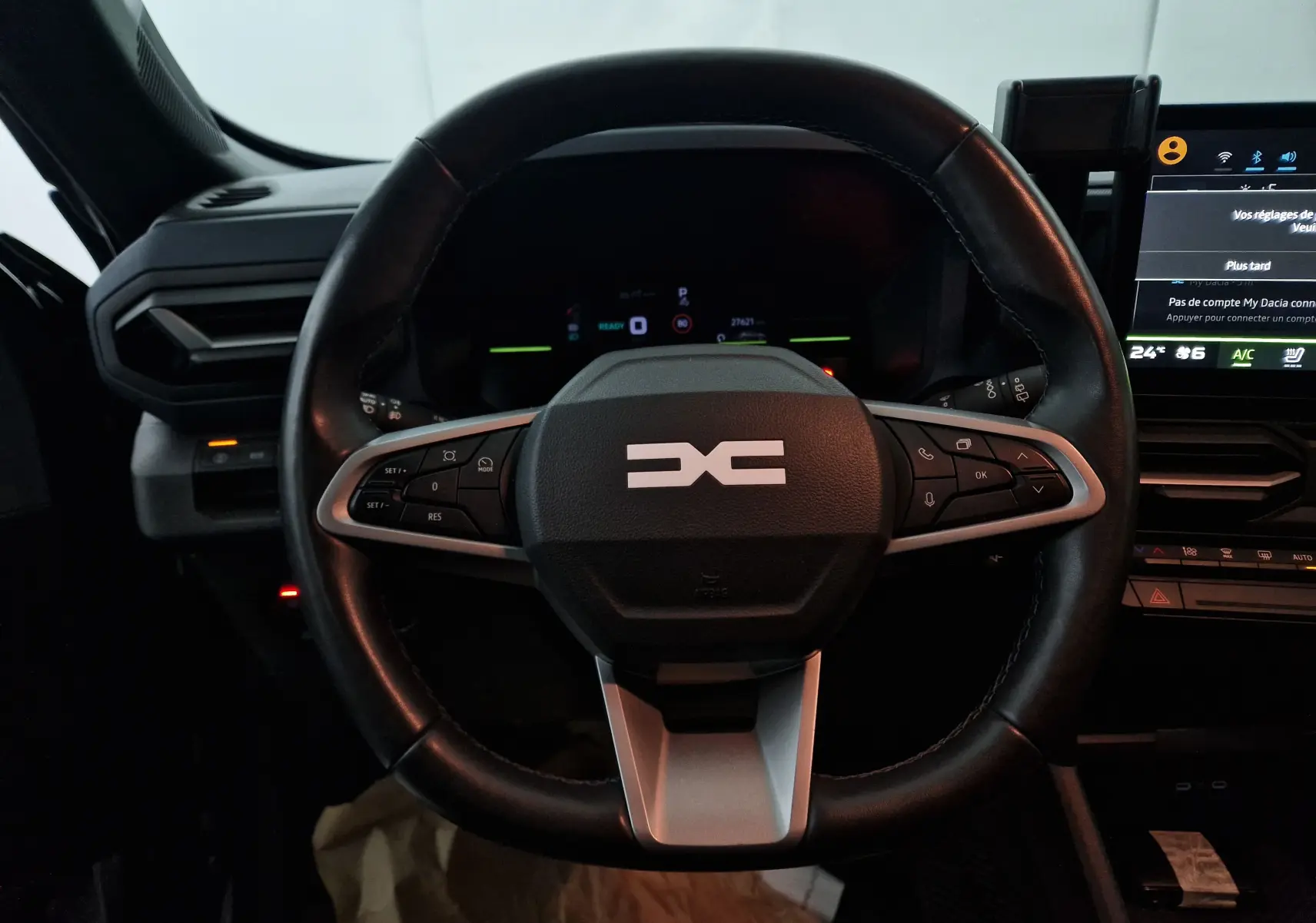 Vue rapprochée du volant noir du Dacia Duster 2024 hybride, avec commandes intégrées et tableau de bord digital en arrière-plan.