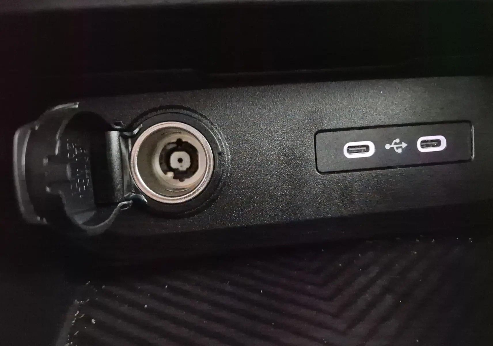 Prise allume-cigare ouverte et deux ports USB-C visibles sur la console centrale noire du Dacia Duster 2024.