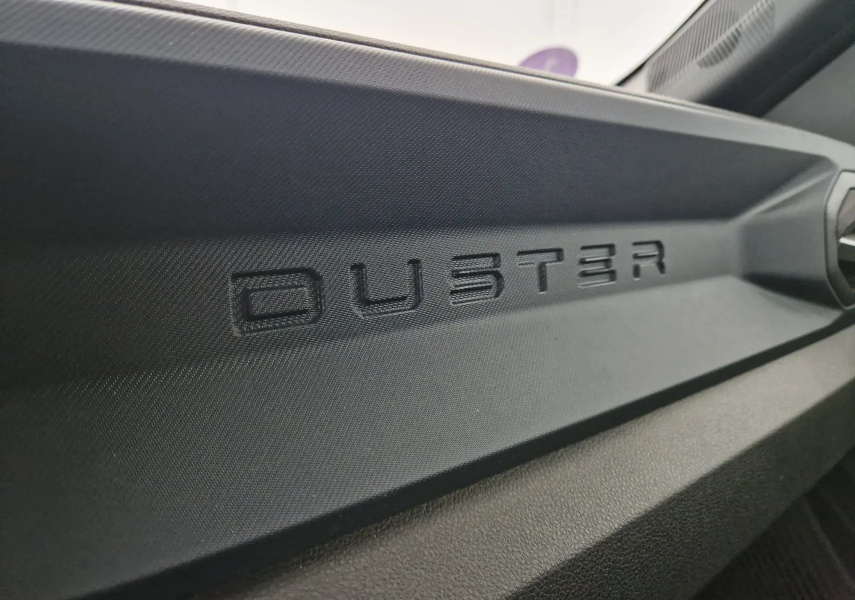 Gros plan sur le logo DUSTER en relief sur la planche de bord noire intérieure du Dacia Duster 2024.