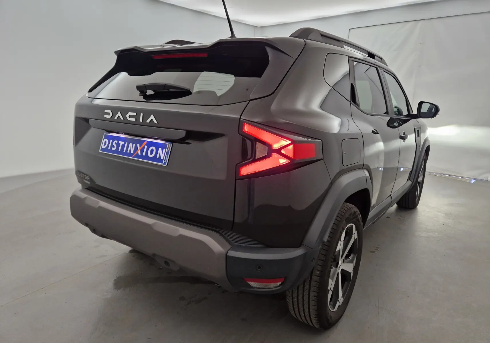 Vue 3/4 arrière droite du Dacia Duster 2024 noir hybride avec feux arrière allumés dans un studio blanc.