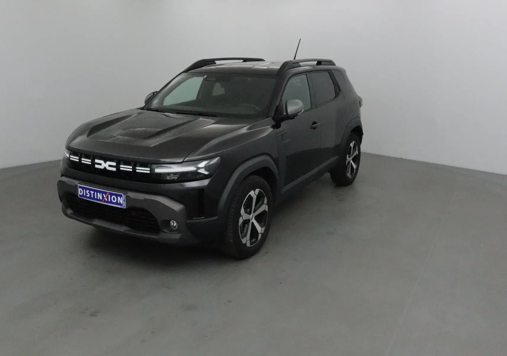 Dacia Duster noir 2024 en 3/4 avant droit, avec jantes alliage et barres de toit visibles.