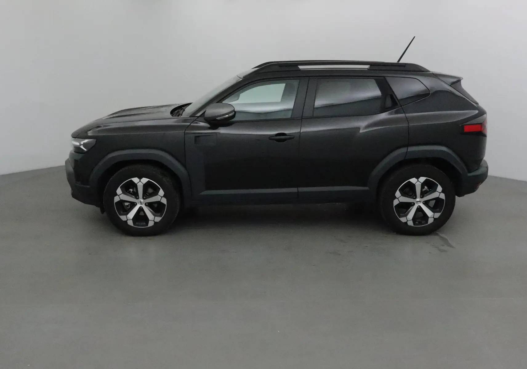 Profil côté gauche du SUV Dacia Duster 2024 noir, avec jantes alliage et barres de toit visibles.