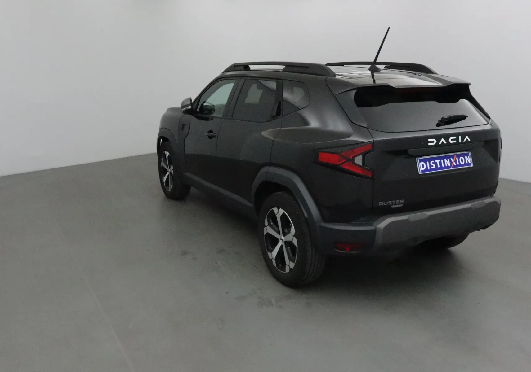 Vue 3/4 arrière droite du Dacia Duster noir 2024 avec feux arrière en forme de flèche et jantes alliage bicolores.