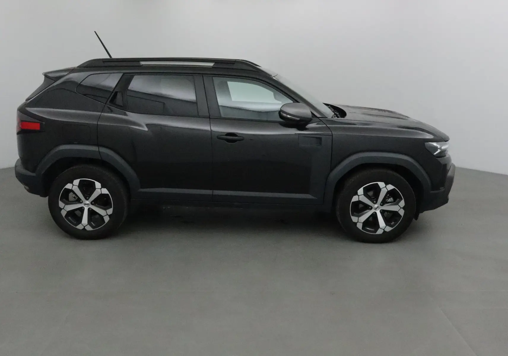 Profil côté gauche du Dacia Duster 2024 noir, version hybride 4x2 avec lignes anguleuses et toit noir contrastant.