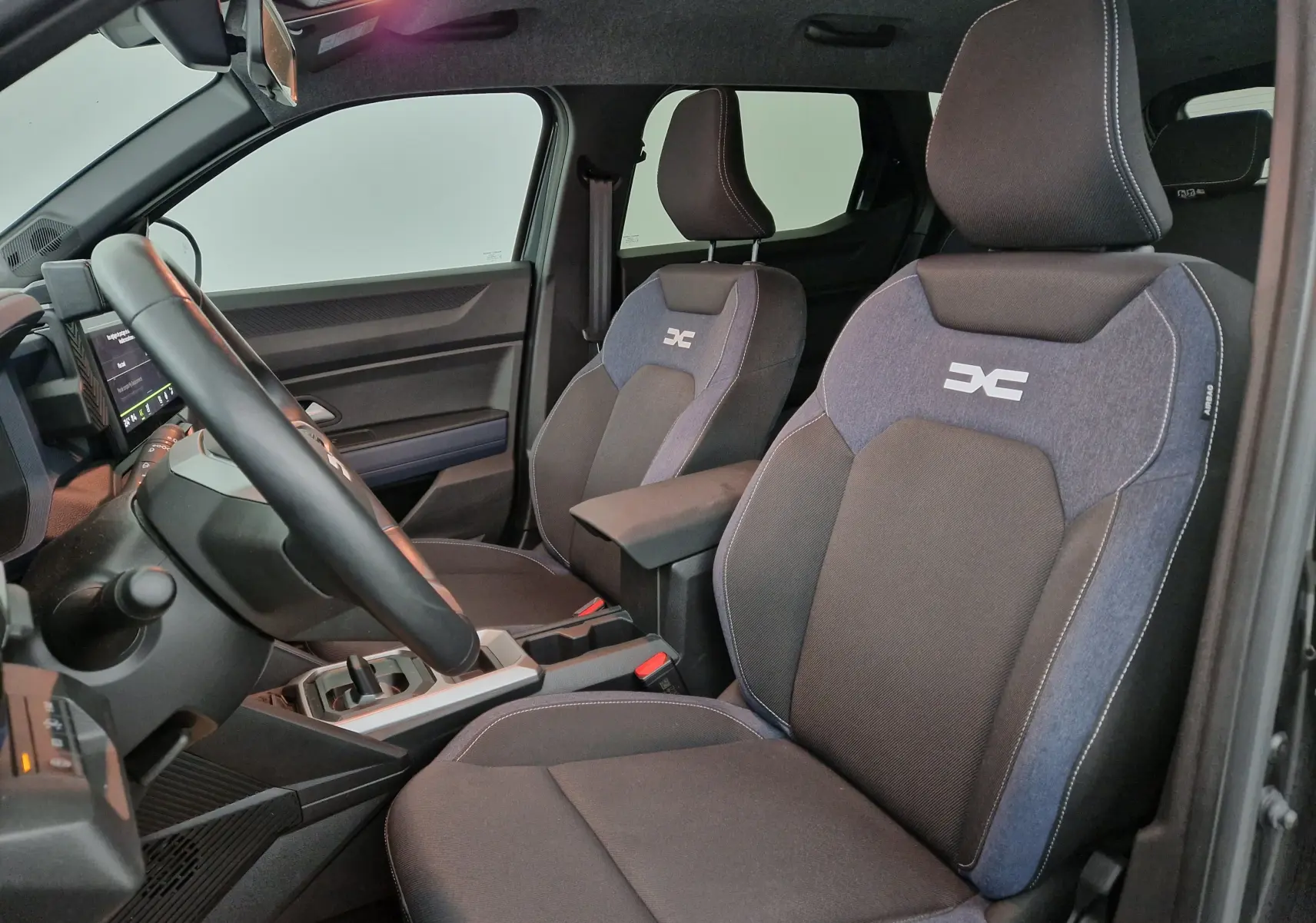 Vue intérieure côté conducteur du Dacia Duster 2024 avec sièges tissu bicolore et logo distinctif brodé.