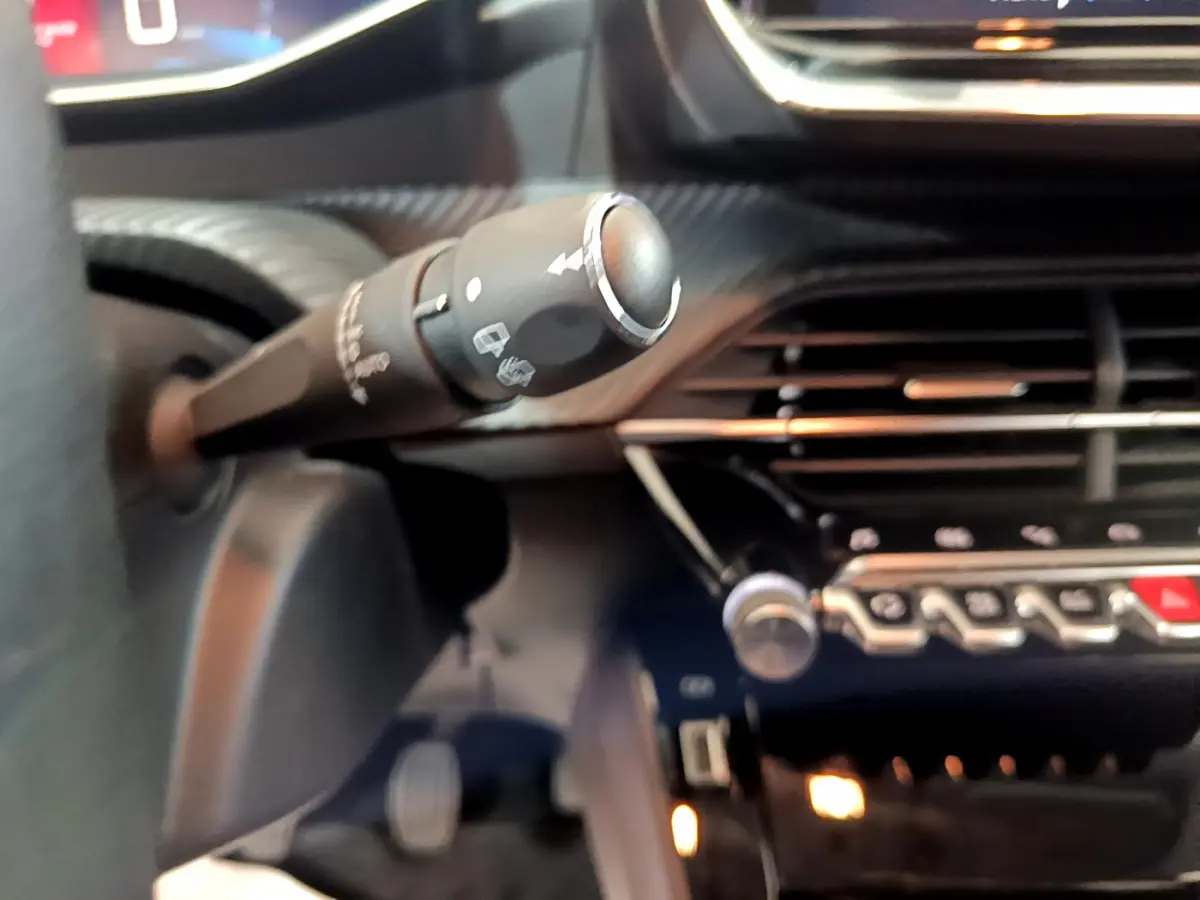 Gros plan sur la commande d’essuie-glace et la console centrale noire du tableau de bord d’une Peugeot 208 gris clair.