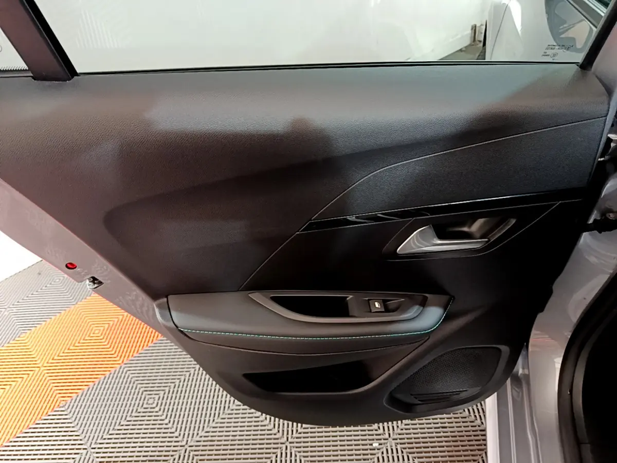 Vue rapprochée de la porte arrière droite gris clair de la Peugeot 208 avec poignée et bouton de vitre électrique.