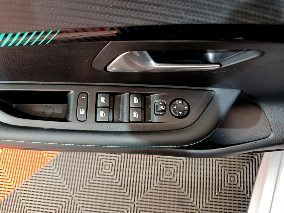 Gros plan sur la commande des vitres électriques et rétroviseurs côté conducteur d'une Peugeot 208 gris clair, porte ouverte.
