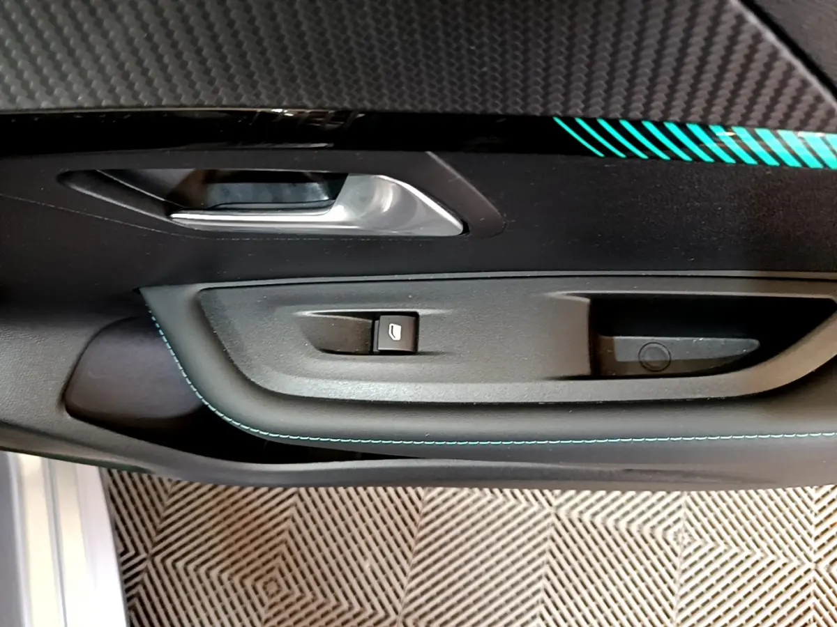 Gros plan sur la poignée intérieure et le bouton de lève-vitre côté conducteur d'une Peugeot 208 gris clair, finition Allure Business.