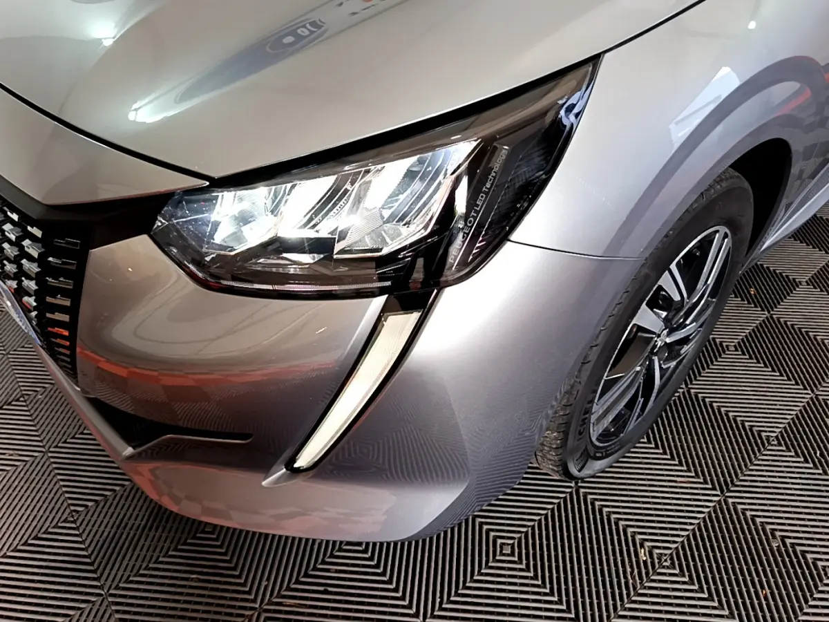 Gros plan sur l'avant droit gris clair d'une Peugeot 208 2020, mettant en valeur le phare LED et la jante alliage.