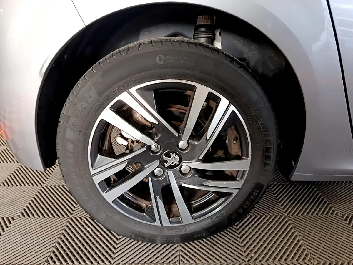 Gros plan sur la roue avant droite d'une Peugeot 208 gris clair, mettant en valeur la jante alliage noire et argentée.