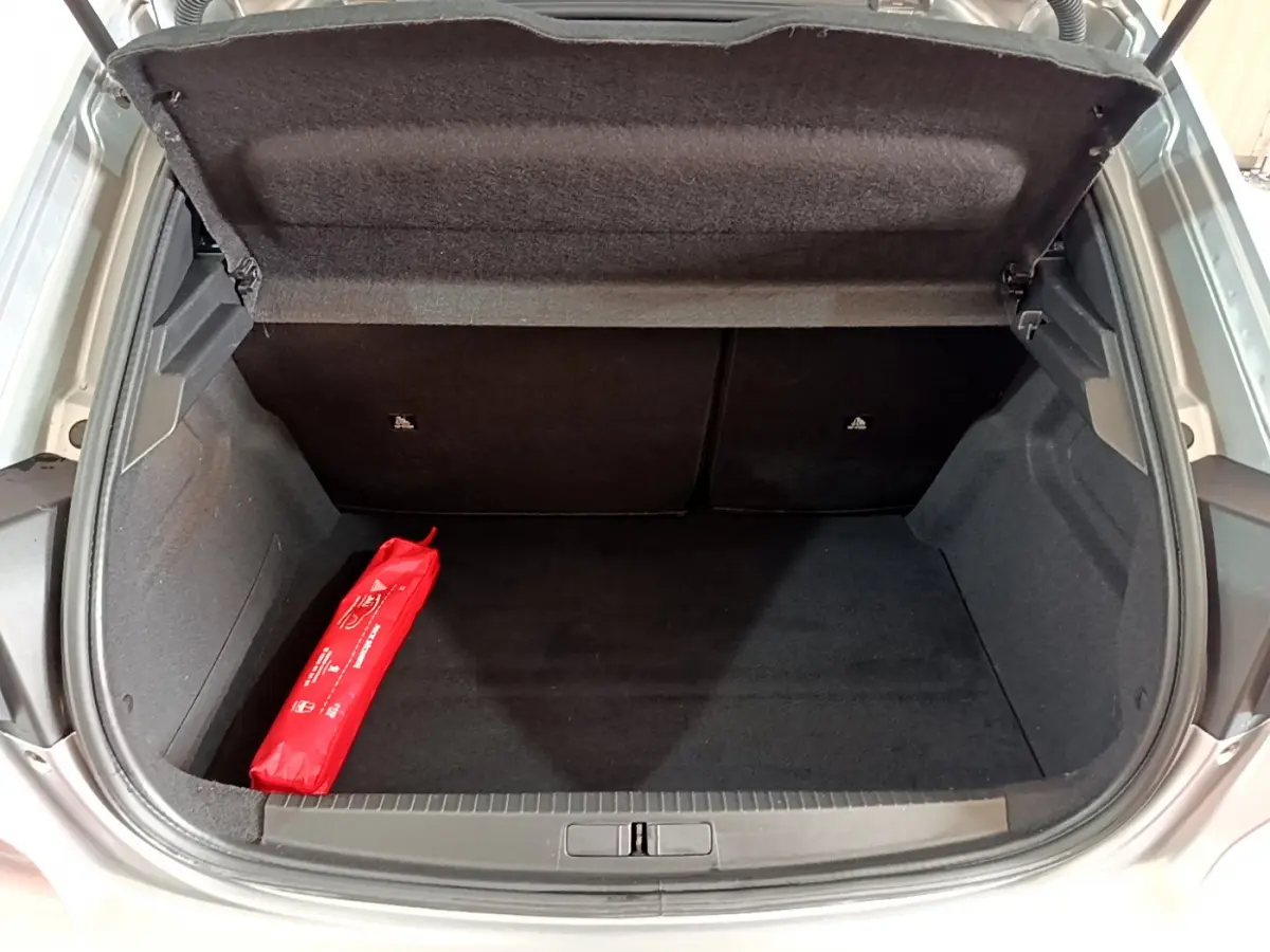 Coffre ouvert d'une Peugeot 208 gris clair, vue de l'arrière montrant un espace vide avec une trousse de secours rouge.