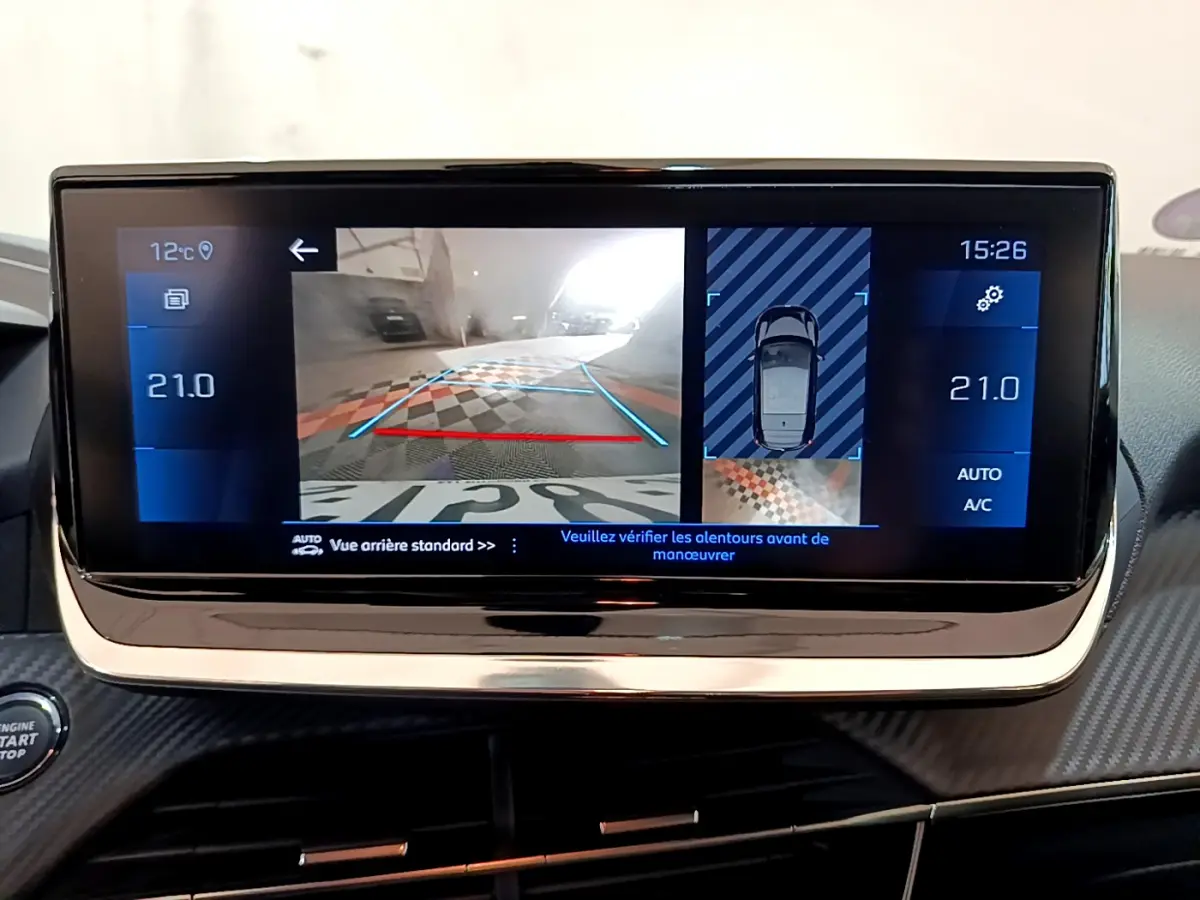 Écran tactile central affichant la caméra de recul et l'aide au stationnement dans une Peugeot 208 gris clair, vue intérieure.