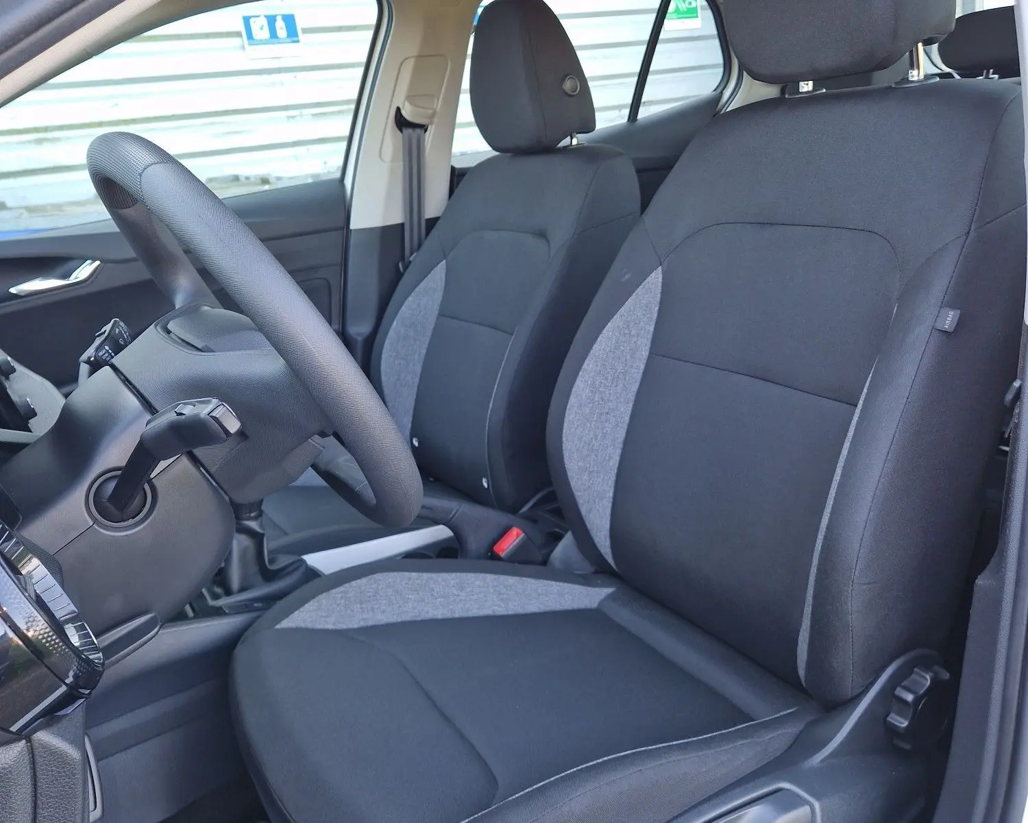 Vue intérieure côté gauche de la Skoda Fabia Berline Active 2022 blanche, montrant les sièges avant en tissu noir et gris.