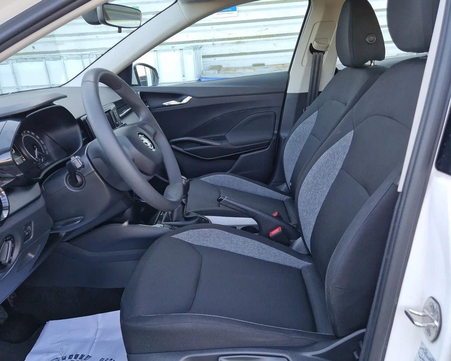 Vue intérieure côté conducteur de la Skoda Fabia Berline Active blanche 2022, sièges tissu noir et gris, volant et tableau de bord visibles.