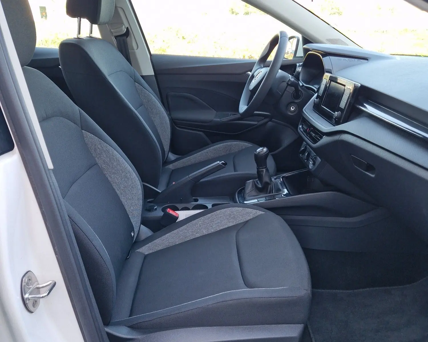 Intérieur côté conducteur d'une Skoda Fabia blanche 2022, avec sièges tissu gris et console centrale manuelle.
