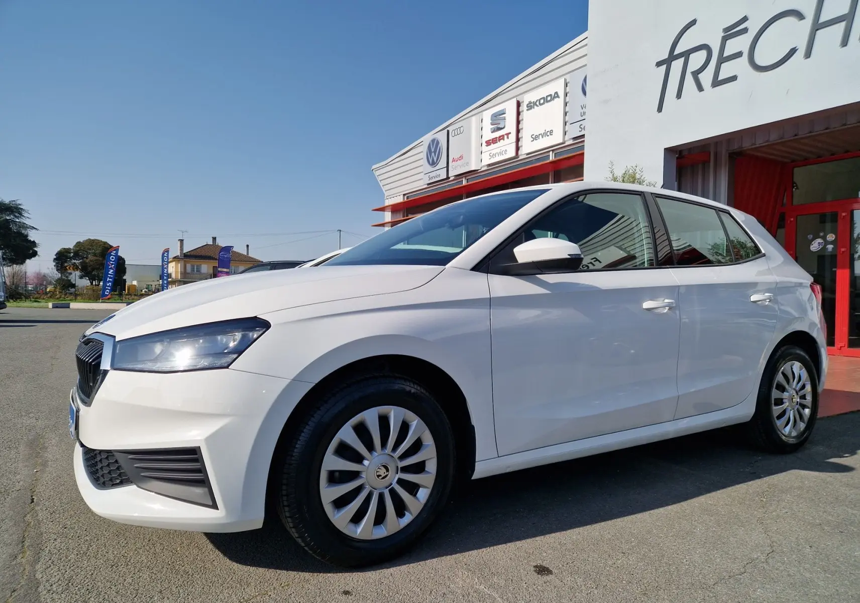 Vue 3/4 avant droite d'une Skoda Fabia Berline Active blanche 2022 stationnée devant un garage.