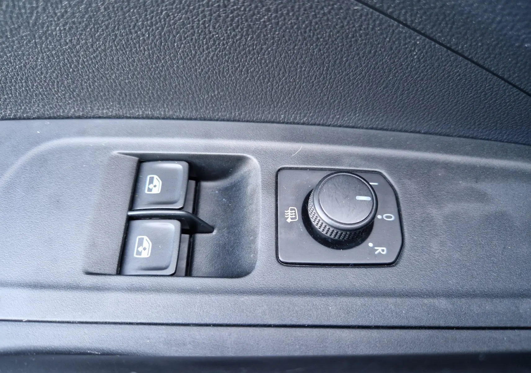 Gros plan sur les commandes de réglage des rétroviseurs et des vitres électriques côté conducteur d'une Skoda Fabia blanche 2022.