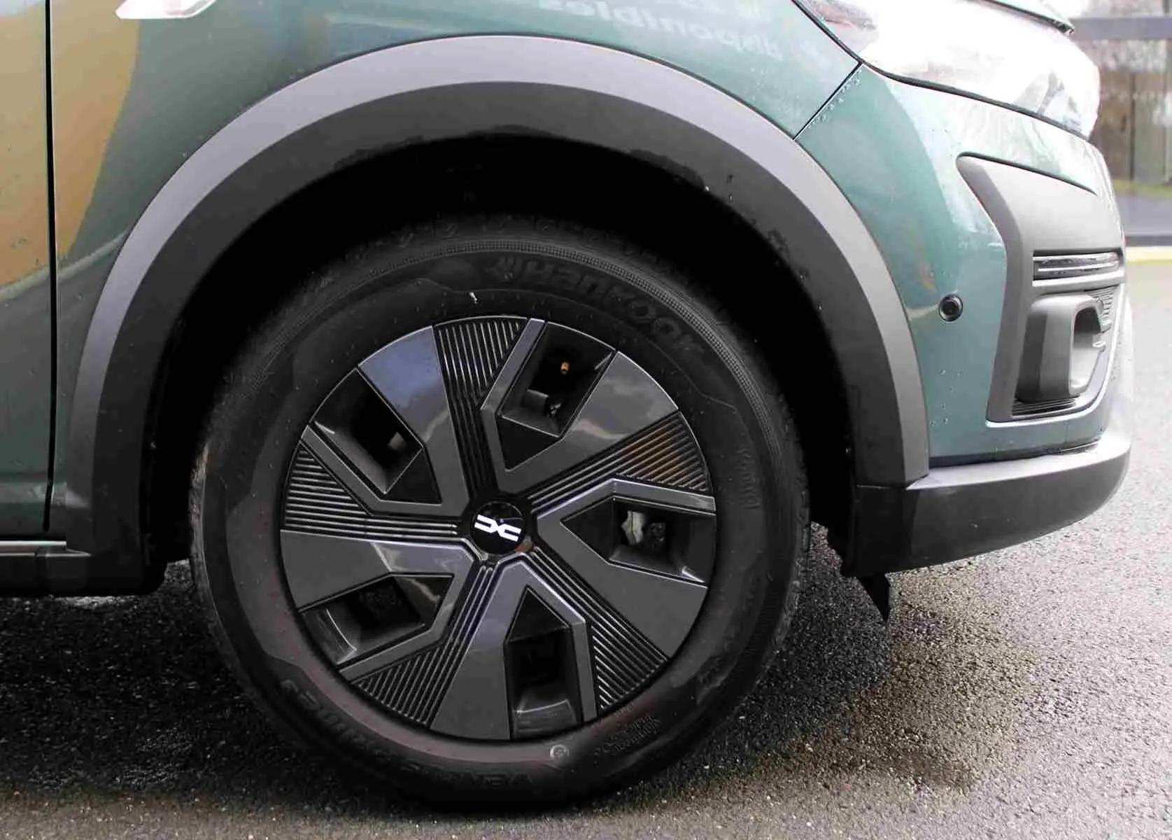 Gros plan sur la roue avant gauche d'un Dacia Jogger vert cèdre métal, avec jante au design géométrique noir et gris.